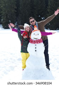 Happy Young  Family Playing In Fresh Snow And Making Snowman At Beautiful Sunny Winter Day Outdoor In Nature With Forest In Background