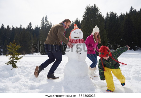 happy young \
family playing in fresh snow and building snowman at beautiful\
sunny winter day outdoor in\
nature