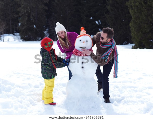 happy young  family playing in fresh snow and\
making snowman at beautiful sunny winter day outdoor in nature with\
forest in background