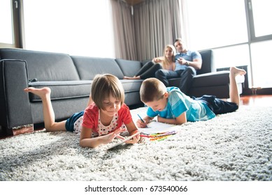 Happy Young Family Playing Together At Home On The Floor Using A Tablet And A Children's Drawing Set