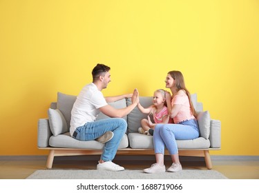 Happy Young Family Playing While Sitting On Sofa Near Color Wall