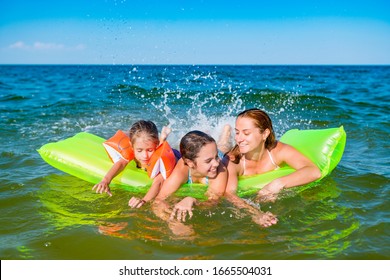 Happy Young Family Positive Mom And Two Little Daughters Swim On A Yellow Air Mattress In The Sea On A Sunny Summer Day During Vacation. Vacation Concept Abroad. Copyspace