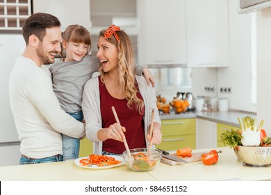 Happy young family preparing lunch in the kitchen and enjoying together.
