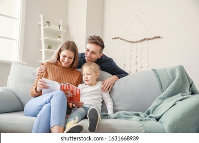 Happy Young Family Reading Fashion Magazine While Sitting On Sofa At Home