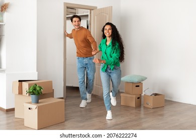 Happy Young Family Running In New Apartment, Young Couple Bought New House. Smiling Happy Guy And Lady Walking Into Big Modern Home, Holding Hands. Real Estate Dwelling, Loan And Mortgage Concept