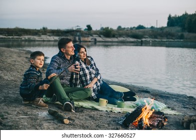  Happy young family sitting around the campfire on the beach at night fall, mother, father, son