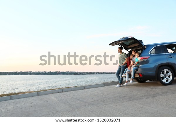 Happy
young family sitting in car trunk on
riverside