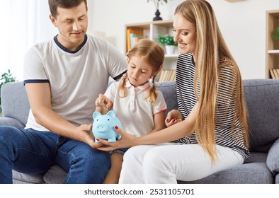 Happy young family sitting on couch together with parents holding blue piggy bank in their hands and little preteen daughter putting coins in moneybox. Planning family budget, economy and saving up. - Powered by Shutterstock