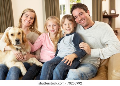 Happy Young Family Sitting On Sofa Holding A Dog