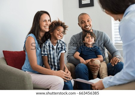 Happy young family sitting on couch and talking with family counselor. Smiling parents with adopted children discussing with counselor. Multiethnic family meeting a financial agent.