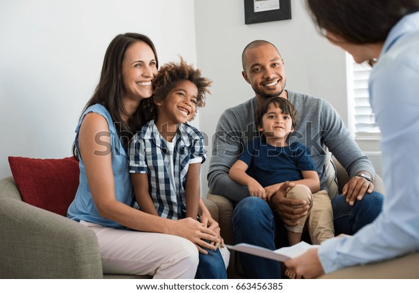 Happy young\
family sitting on couch and talking with family counselor. Smiling\
parents with adopted children discussing with counselor.\
Multiethnic family meeting a financial\
agent.