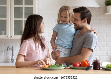 Happy Young Family With Small Preschooler Daughter Have Fun Preparing Breakfast Or Lunch In Kitchen, Smiling Parents Have Fun With Little Girl Child Cook Salad Chop Vegetables, Healthy Life Concept