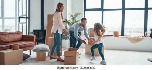 Happy Young Family Smiling And Unboxing Their Stuff While Moving Into A New Apartment