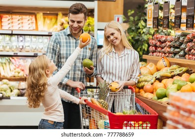 Happy young family standing with a trolley and choosing fruits at the supermarket - Powered by Shutterstock