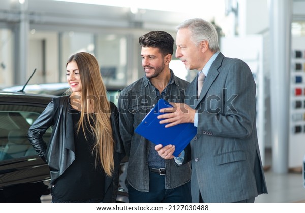 Happy young family talking to the salesman and\
choosing their new car in a\
showroom