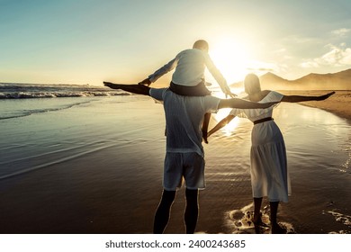 Happy young family of three spending free time outdoors, walking and having fun on seaside. Back view. Copy space. Island vibes. Sunset light. Vacation.