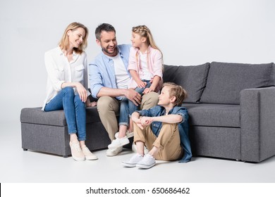 Happy Young Family With Two Children Sitting Together On Sofa And Smiling