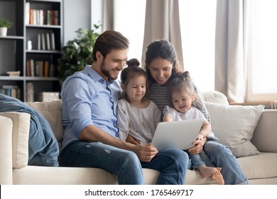 Happy Young Family With Two Little Daughters Using Laptop Together, Smiling Mother And Father With Adorable Preschool Girls Looking At Screen, Watching Cartoons, Shopping Online, Making Video Call