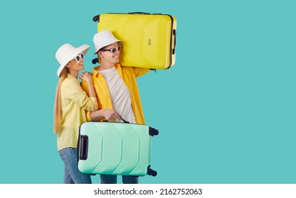 Happy Young Family With Two Suitcases Going On Summer Holiday Together. Millennial Couple In Yellow Shirts, Hats And Sun Glasses Look To Side At Turquoise Copyspace Background. Travel Vacation Concept