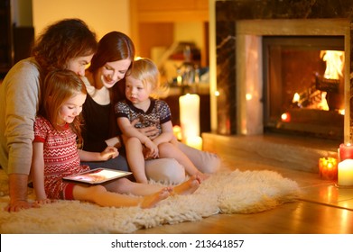 Happy Young Family Using A Tablet Pc At Home By A Fireplace In Warm And Cozy Living Room On Winter Day