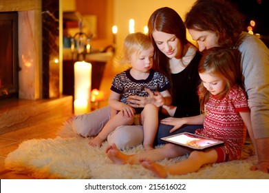 Happy Young Family Using A Tablet Pc At Home By A Fireplace In Warm And Cozy Living Room On Winter Day