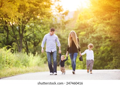 Happy Young Family Walking Down The Road Outside In Green Nature.