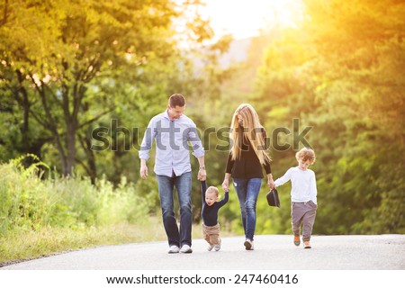 Happy young family walking down the road outside in green nature.