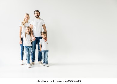 Happy Young Family In White T-shirts And Denim Pants Looking At Camera Isolated On White