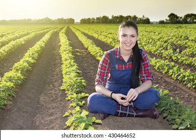 Happy young farmer girl sitting in soybean field in early summertime