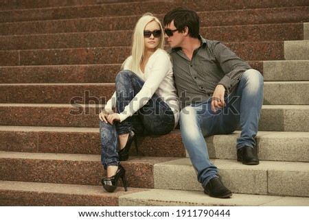 Happy young fashion couple on the steps Stylish trendy man and woman in sunglasses and blue jeans