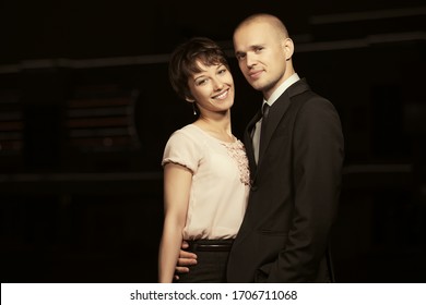 Happy Young Fashion Couple Walking On City Street At Night Stylish Man In Black Suit Jacket And Woman In Light Pink Blouse And Skirt