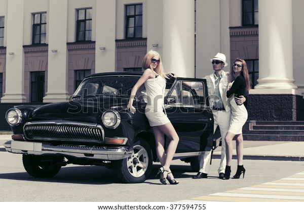 Happy\
young fashion man and women standing by retro\
car