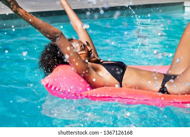 Happy young fashion woman in bikini with rubber inflatable float and having fun with water at swimming pool. Smiling african girl splashing water in resort pool. Beautiful black lady relax at pool.