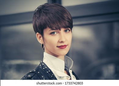 Happy young fashion woman walking on city street Stylish female model in black leather jacket with pixie hair style