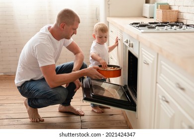Happy young father  and cute boy son  bake apple pie in kitchen oven. Smiling father  teaching child take tray with aple pie dessert make cakes out oven stove cook at home, family bakery concept