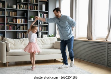 Happy young father dance with cute little daughter princess wearing crown and beautiful skirt, smiling dad have fun engaged in funny activity playing with small preschooler girl child at home