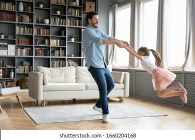 Happy young father have fun with little preschooler daughter relax together at home, overjoyed dad dance and swirl sway with excited small girl child, enjoy family weekend in living room