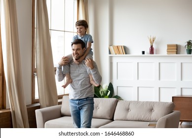 Happy young father holding on shoulders joyful son, having fun together in living room. Smiling handsome dad playing with adorable laughing school boy kid, enjoying weekend active time at home. - Shutterstock ID 1646468860