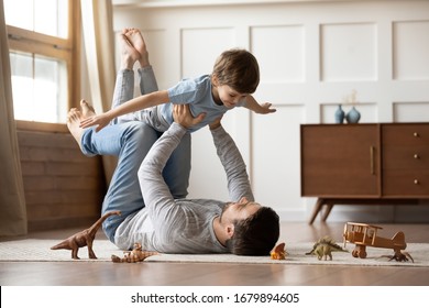 Happy young father lying on floor in living room hold fly with little preschooler son engaged in funny game together, loving dad relax playing with small boy child, enjoy family weekend at home - Shutterstock ID 1679894605