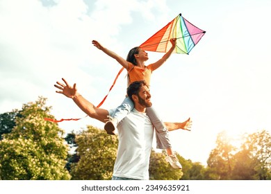 Happy young father playing with his beloved daughter with an air colorful kite in a meadow in the park, having fun together on a warm sunny weekend. - Powered by Shutterstock