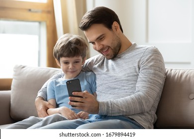 Happy young father sit relax on couch in living room with little son make selfie on smartphone, dad rest on sofa at home with small boy child watch video on cellphone enjoy leisure weekend together - Powered by Shutterstock