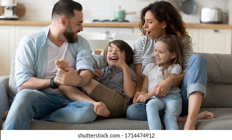 Happy young father tickling little kid boy son while smiling mother cuddling small daughter on couch. Cheerful full family of four having fun on sofa, enjoying weekend holiday time together at home.