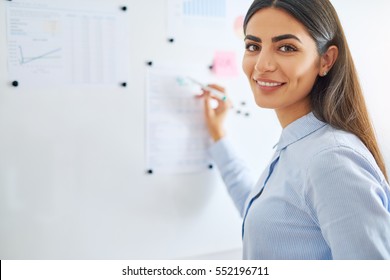Happy young female business woman or teacher writing on white board with erasable marker