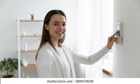 Happy young female client looking at camera, pressing buttons on smart house system. Smiling millennial woman using indoors temperature controller or air conditioning, setting alarm password. - Shutterstock ID 1809678100