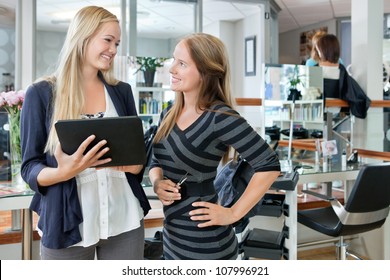 Happy young female customer looking at hairdresser while holding digital tablet - Powered by Shutterstock