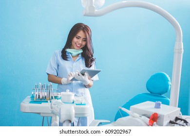 Happy Young Female Dentist With Tablet Over Medical Office Clinic