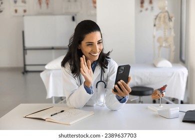 Happy young female doctor woman talking on video call to patient, waving greeting hello at smartphone, giving help, assistance, online consultation. Medical specialist speaking on Internet conference - Powered by Shutterstock