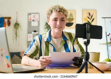 Happy Young Female Employee Or Auditor With Papers Giving Online Training In Home Environment While Sitting By Workplace