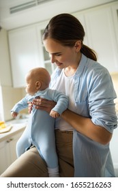 Happy young female holding her little kid while standing at home stock photo