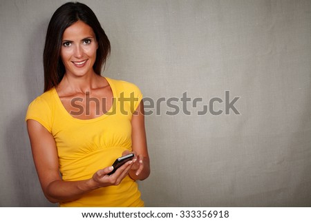 Happy young female holding mobile phone while looking at camera - copy space